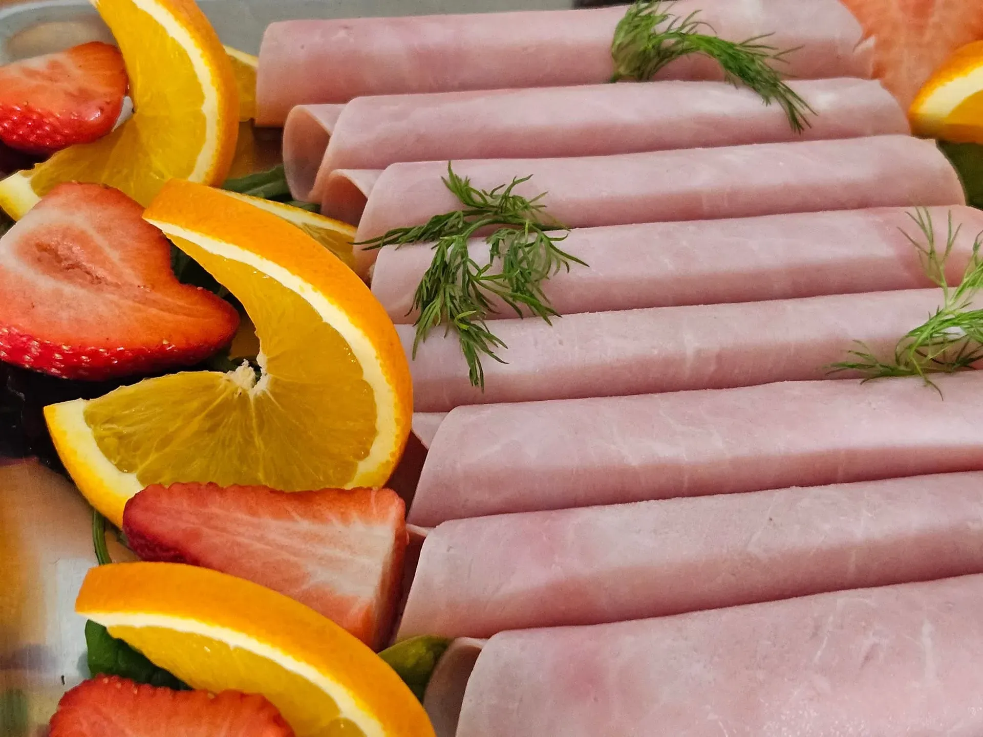Schinkenröllchen garniert mit Orangen, Erdbeeren und Dill